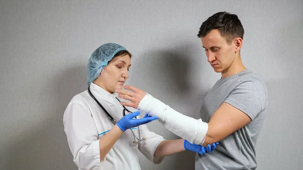 Médico morena examina el antebrazo roto del joven — Foto de Stock