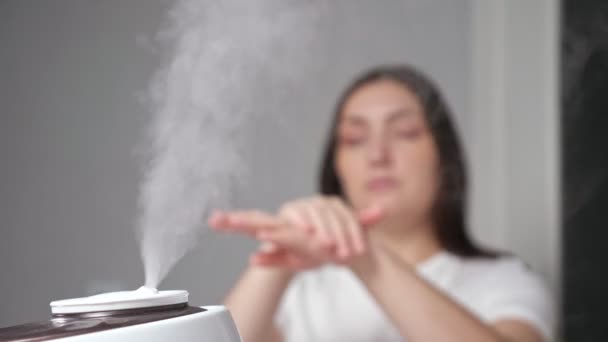 Молода жінка наносить крем на руки, насолоджуючись зволоженим повітрям — стокове відео
