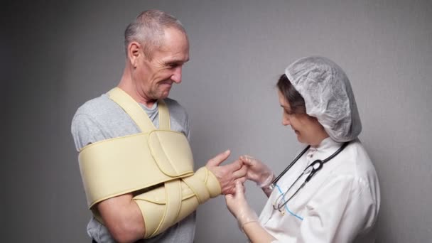 Lady ortopedka kontroluje kosti starého muže s obvazem — Stock video