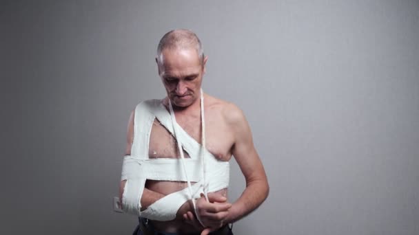 Старший чоловік з бинтом оглядає зламане плече на стіні — стокове відео