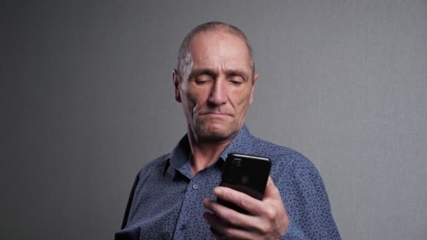 Starší muž čte novinky v mobilním telefonu na šedém pozadí