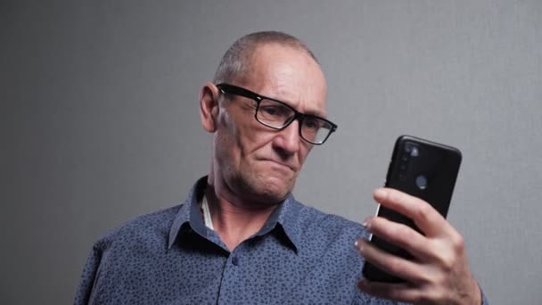 Старший в очках пытается прочитать сообщение на смартфоне — стоковое видео
