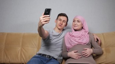 Genç ebeveynler video aracılığıyla konuşuyor. Hamile karnı okşayarak.