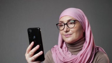 Tesettürlü genç Müslüman kadın telefon kullanarak programı izlerken gülümsüyor