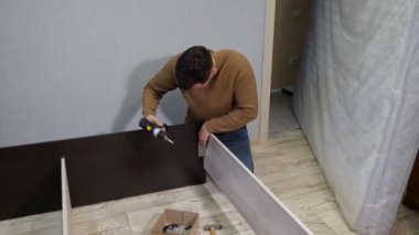 Kahverengi kazaklı genç adam yatağı tornavidayla birleştiriyor.