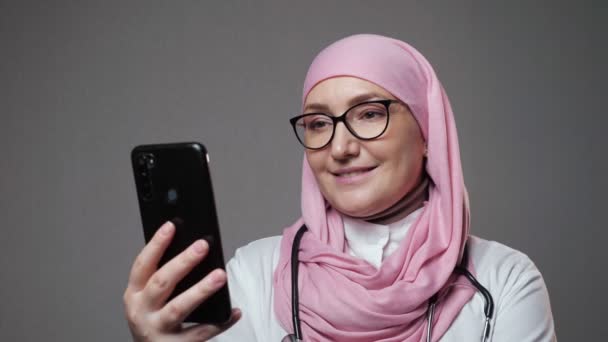 Мусульманська жінка-лікар посміхається серфінгу в Інтернеті через телефон — стокове відео