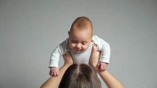 Ung mor leker med kärlek med barnet mot grå vägg — Stockvideo