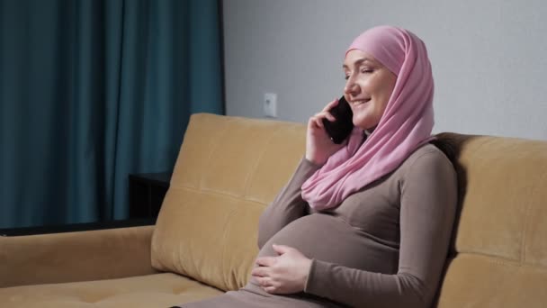 Muslim woman caresses pregnant belly talking via phone — Stockvideo