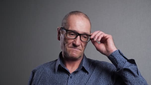 Senior man takes off glasses rubbing eyes on grey background — Stock Video