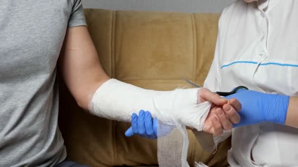 Enfermera corta vendaje de yeso de brazo curado de hombre joven — Vídeos de Stock