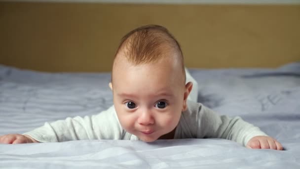 Baby lies and tries to crawl on blanket looking into camera — Stock Video