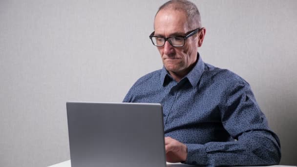 Hombre mayor trabaja en la computadora sentado en el escritorio blanco en la oficina — Vídeo de stock