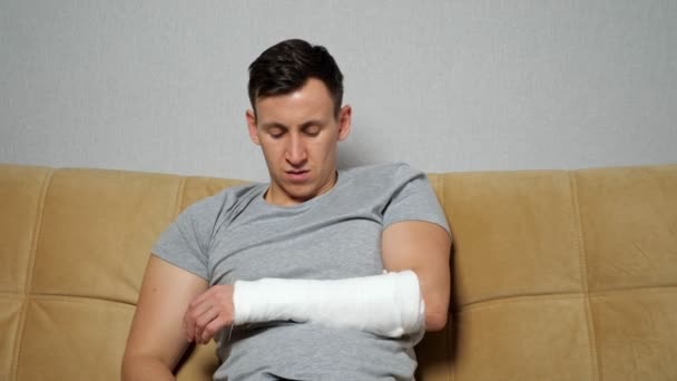 El hombre toca el brazo herido en banda de yeso y suspira cansadamente — Vídeo de stock
