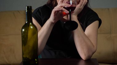 Tanımlanamayan, gergin yüzlü, çakırkeyif kadın şarap içer.