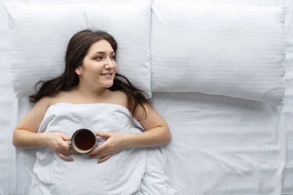 Vista superior de la mujer joven en la cama con taza de café, espacio para copiar — Foto de Stock