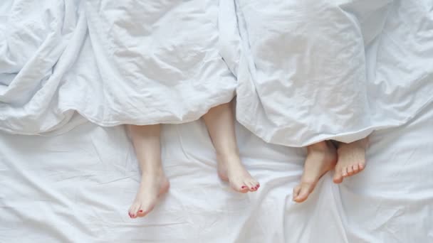 Jovem casal cruza pernas preso fora de lençol deitado na cama — Vídeo de Stock