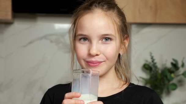 Девочка-подросток пьет свежее молоко, облизывая белые усы дома. — стоковое видео