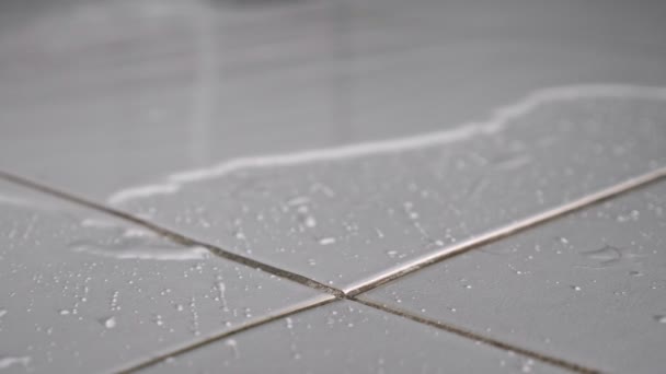 Ροές νερού στο πάτωμα που καλύπτει λευκό κεραμικό πλακίδιο στο μπάνιο — Αρχείο Βίντεο