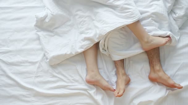 Пара ласкает друг друга лежа в постели на белых простынях — стоковое видео