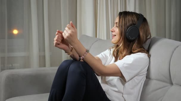 Mujer alegre disfruta de la música en los auriculares sentados en el sofá — Vídeos de Stock