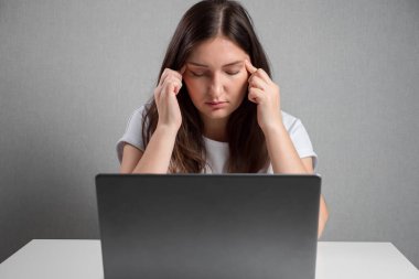 young woman massaging temples while sitting in front of laptop