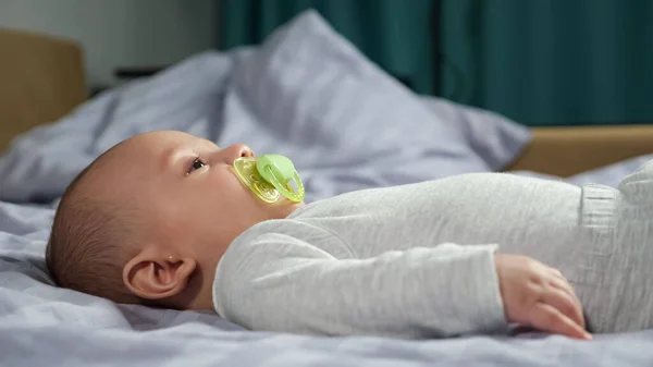 เด็กทารกตัวเล็กนอนบนเตียงอ่อนและเคลื่อนไหวด้วยหุ่นในปาก — ภาพถ่ายสต็อก