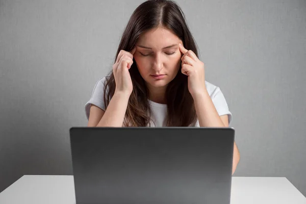 Young woman massaging temples while sitting in front of laptop — Fotografia de Stock