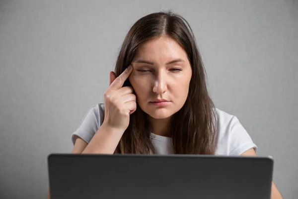 Young brunette woman sitting at the laptop squints eyes — Stockfoto