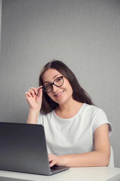 Young brunette woman in glasses sitting in front of a laptop and smiling, copy space — Fotografia de Stock