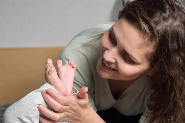 Moms love for the baby. Brunette woman holding legs of baby — Photo