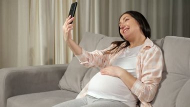Woman talks via videocall using phone and stroking belly