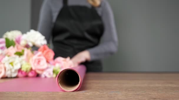 Florist unrolls pink wrapping paper on table to put flowers — стоковое видео