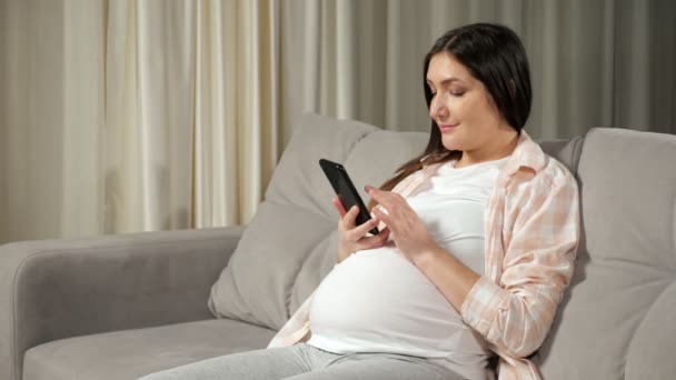 Pregnant woman scrolls through social media via smartphone — стоковое видео