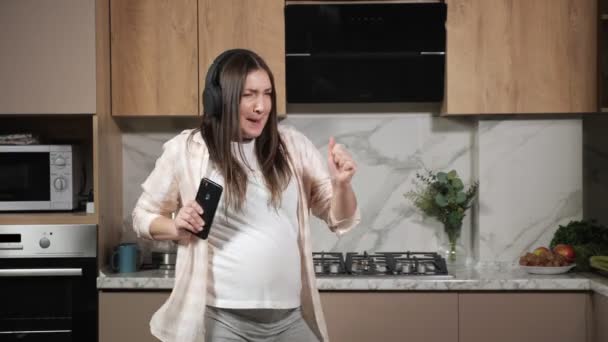 Gravid kvinna sjunger och dansar med telefon och hörlurar — Stockvideo