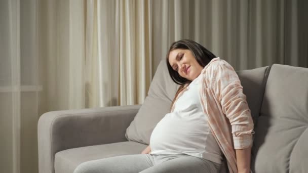 Mujer morena embarazada lucha para ponerse de pie desde el sofá — Vídeos de Stock