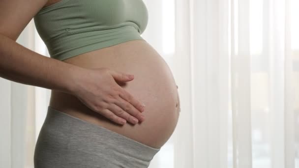 Женщина наносит увлажняющий крем на беременный живот — стоковое видео