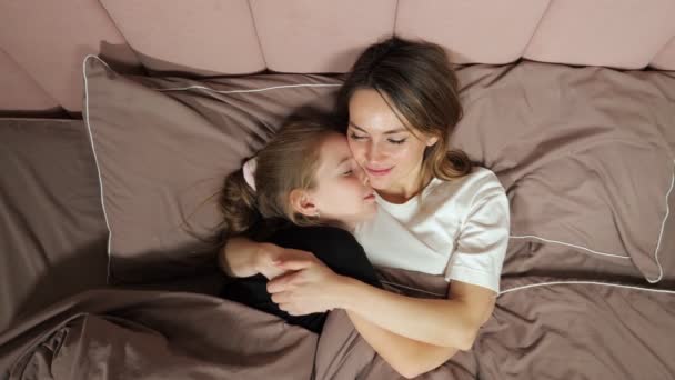 Mother and daughter prepare to sleep hugging in bed at home — Stock video