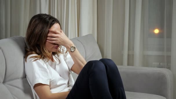 Vrouw behandelt hoofdpijn zittend op de bank in de woonkamer — Stockvideo