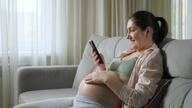 Hamile kadın internet haberlerini akıllı telefon kullanarak okuyor.