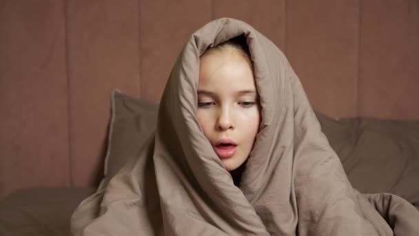 Άρρωστο έφηβο κορίτσι κάθεται στο κρεβάτι καλύπτει το κεφάλι με ζεστή κουβέρτα — Αρχείο Βίντεο
