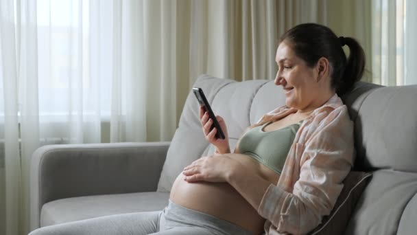 Pregnant woman reads news in internet using smartphone — Stock Video