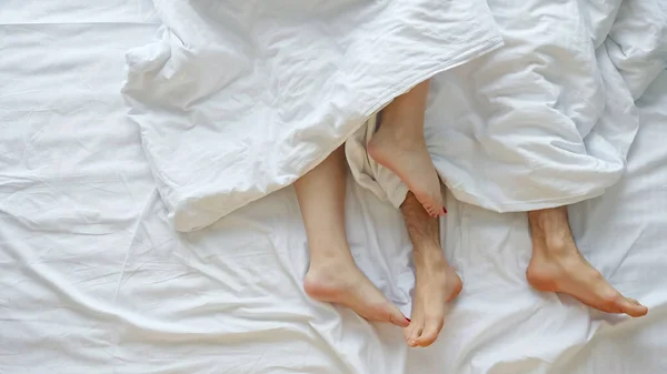 Couple caresses each other lying in bed on white sheets — Stock Photo, Image