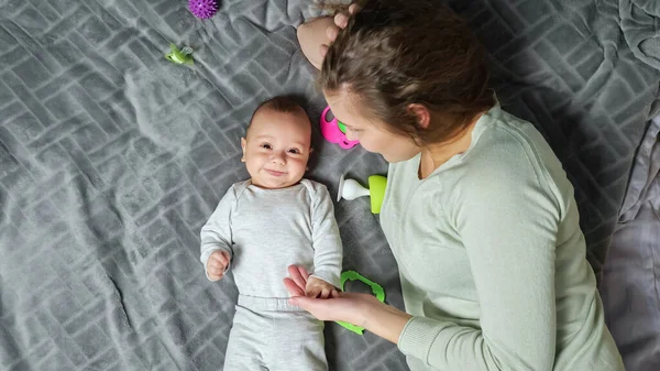 Jeune mère tient la main du fils nouveau-né couché à proximité sur le lit — Photo
