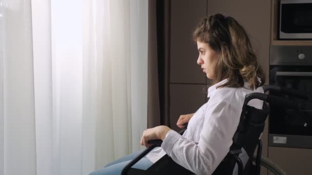 Femme handicapée pensive assise en fauteuil roulant par la fenêtre à la maison — Video