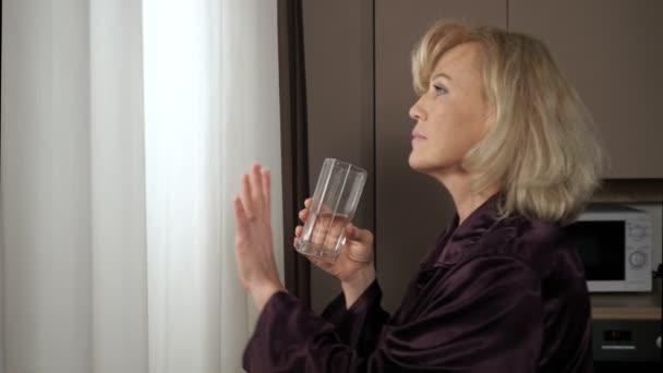 中年女性は窓の外の景色を楽しむ水を飲む — ストック動画