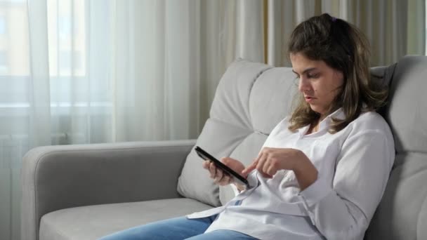 Mujer discapacitada apenas utiliza el teléfono móvil sentado en el sofá — Vídeo de stock