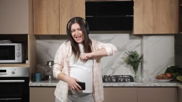 Těhotná žena zpívá a tančí s telefonem a sluchátky — Stock video