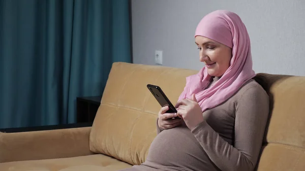 Mujer musulmana embarazada se desplaza por las redes sociales con el teléfono — Foto de Stock