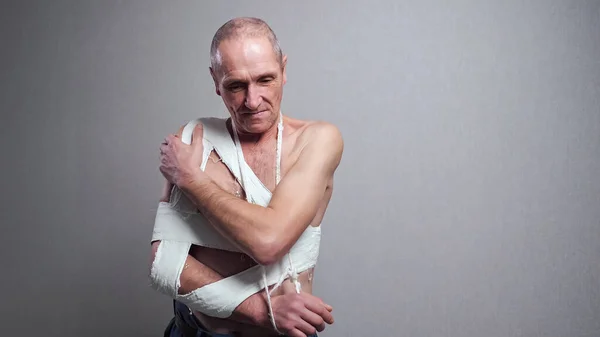 Старший чоловік з бинтом оглядає зламане плече на стіні — стокове фото