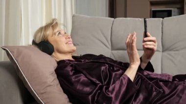 Yaşlı kadın kulaklıkla müzik dinleyerek haber okuyor.
